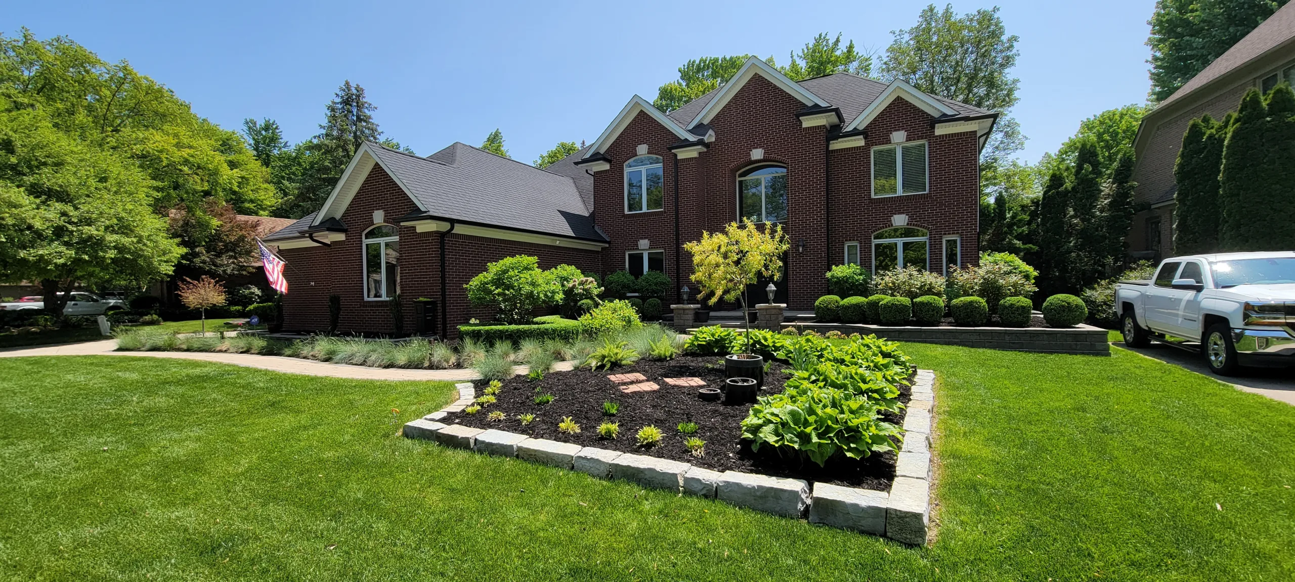 A professionally designed landscape with a variety of plants, trees, and mulch in a backyard in Rochester Hills, Michigan.